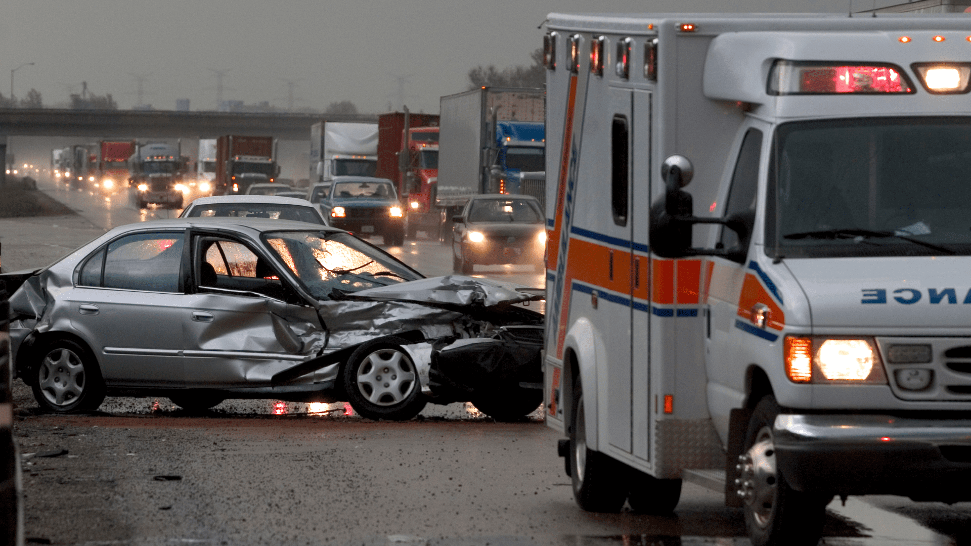 severely damaged car in the background after an accident with an ambulance in the foreground on a highway 