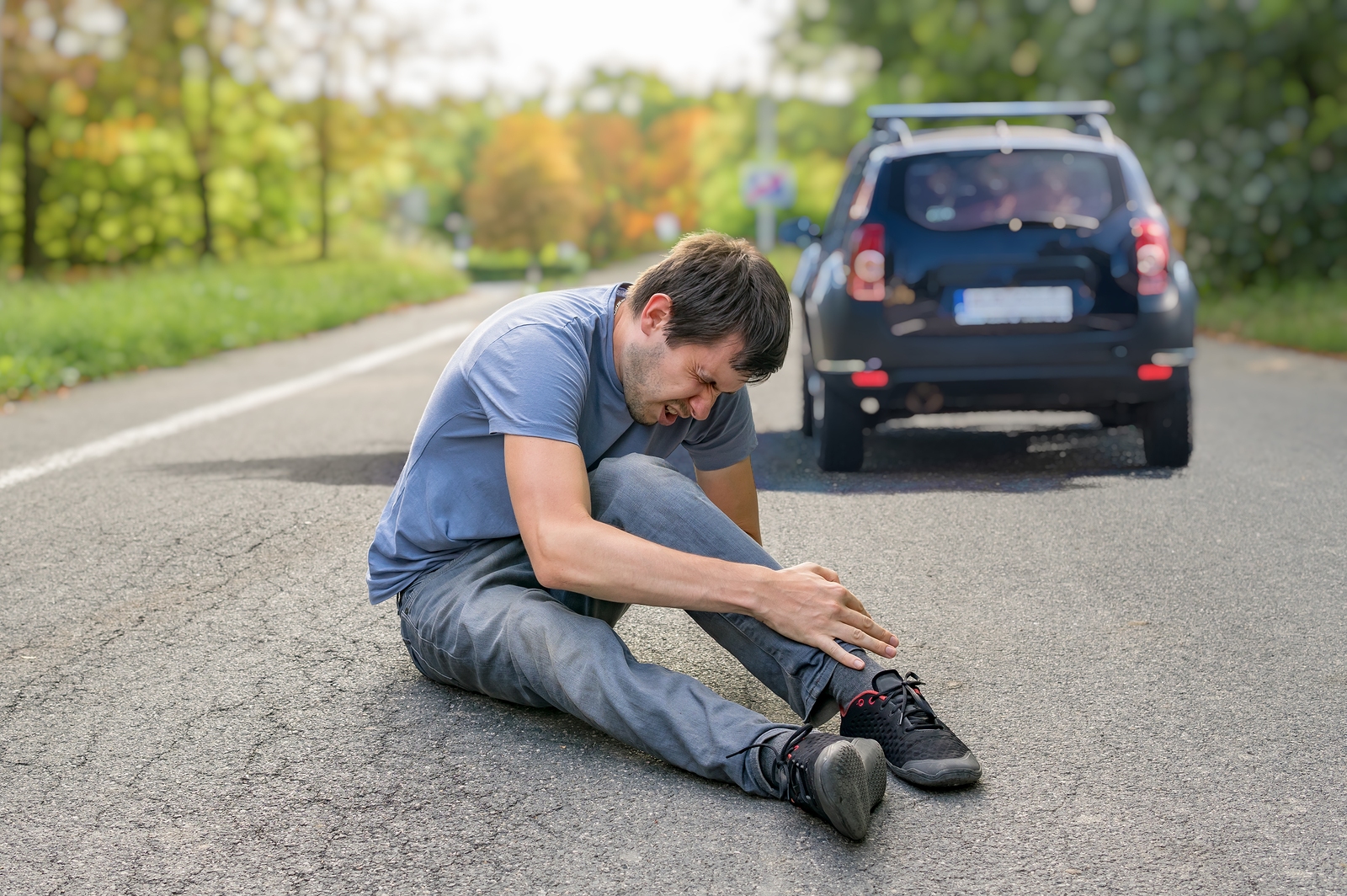 man in pain holding his left after being struck by a black crossover vehicle