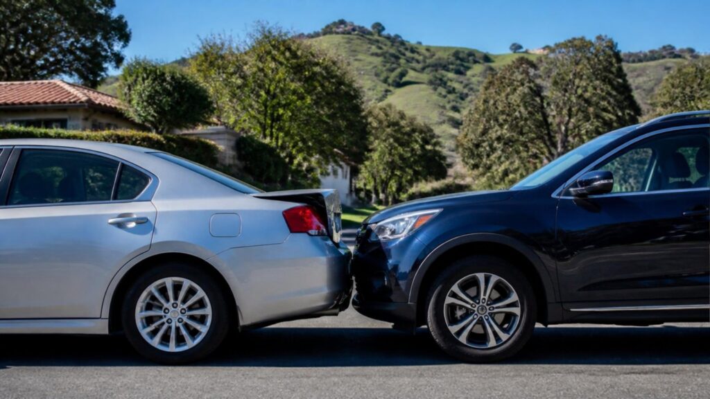 A dark SUV rear-ends a silver sedan on a residential street below green hills