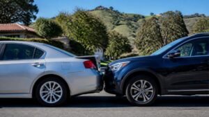A dark SUV rear-ends a silver sedan on a residential street below green hills