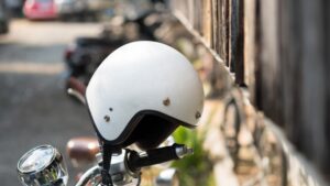 A white open-face motorcycle helmet resting on the handlebar of a parked motorcycle